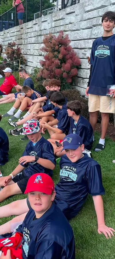 Bluefins players sitting together on the grass in team shirts, watching from the sideline