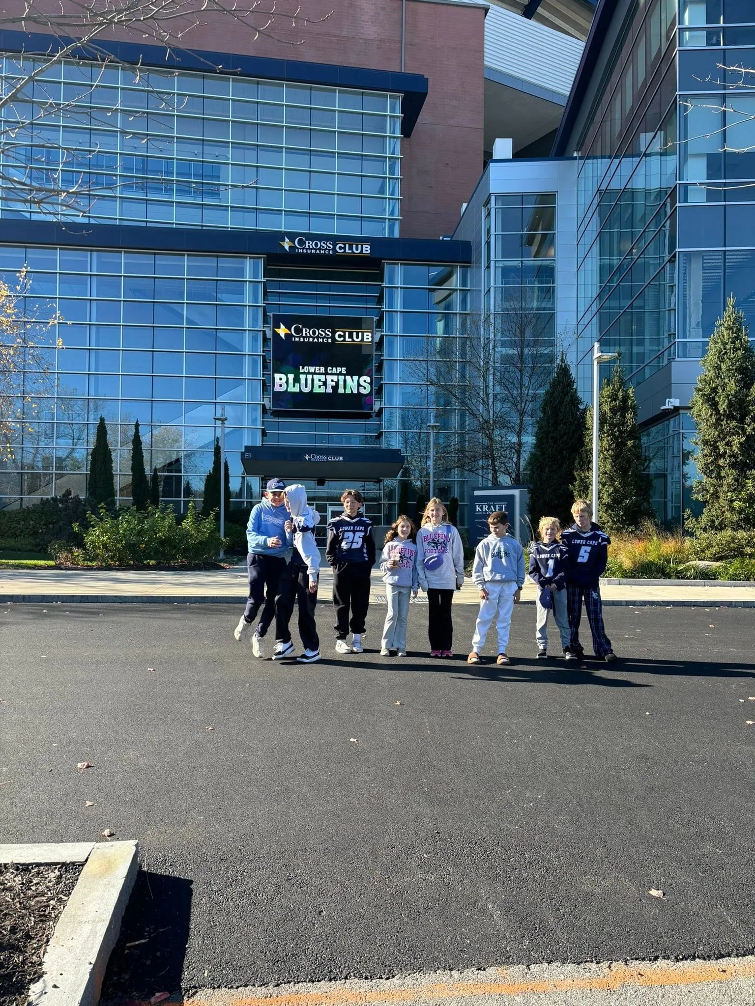 Bluefins players and a coach standing together outside a stadium club entrance, with the club name on the screen behind them